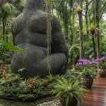 Statue gorille en pierre dans un jardin luxuriant avec des plantes tropicales.